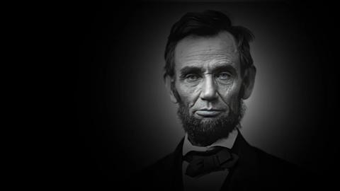 Black-and-white portrait of a man with a beard, wearing a suit and bow tie, set against a dark background.