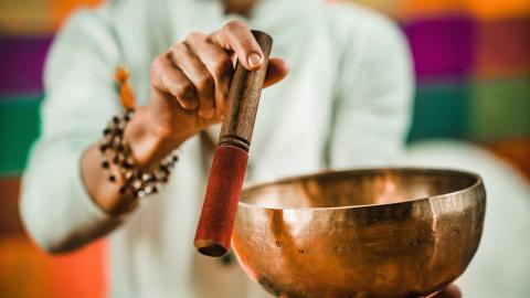 Person using a mallet to play a singing bowl, with colorful background.