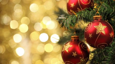 Red Christmas ornaments with gold star patterns hanging on a Christmas tree branch with a golden bokeh background.