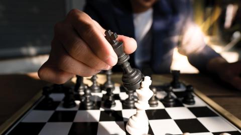 A person moves a black chess piece on a chessboard, captured in dramatic lighting.