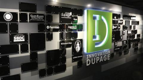 Illuminated Innovation DuPage logo on wall with various partner logos on black plaques.