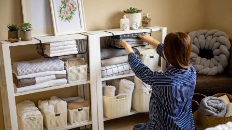 A person in striped pajamas organizing shelves with neatly folded linens and storage baskets in a cozy room.