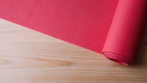 A rolled-up red yoga mat partially unrolled on a light wood floor.