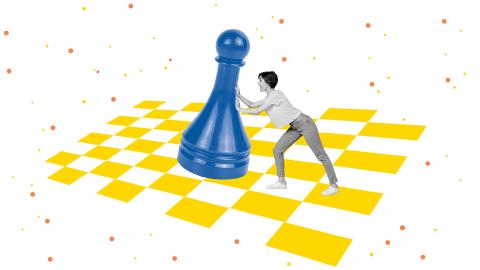 A person pushes a giant blue chess pawn on a yellow checkerboard with scattered dots.