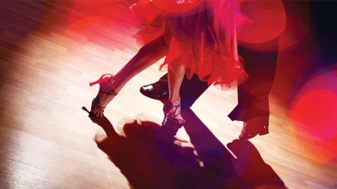 Two people dancing on a wooden floor, wearing elegant shoes, with a red light illuminating their movements.