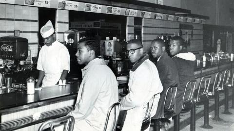 Four Black men sit at a segregated lunch counter as a white worker stands behind the counter, circa 1960s.