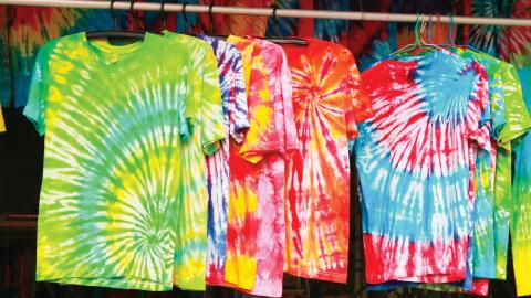 Colorful tie-dye t-shirts with spiral patterns hanging on a rack at a market or shop.