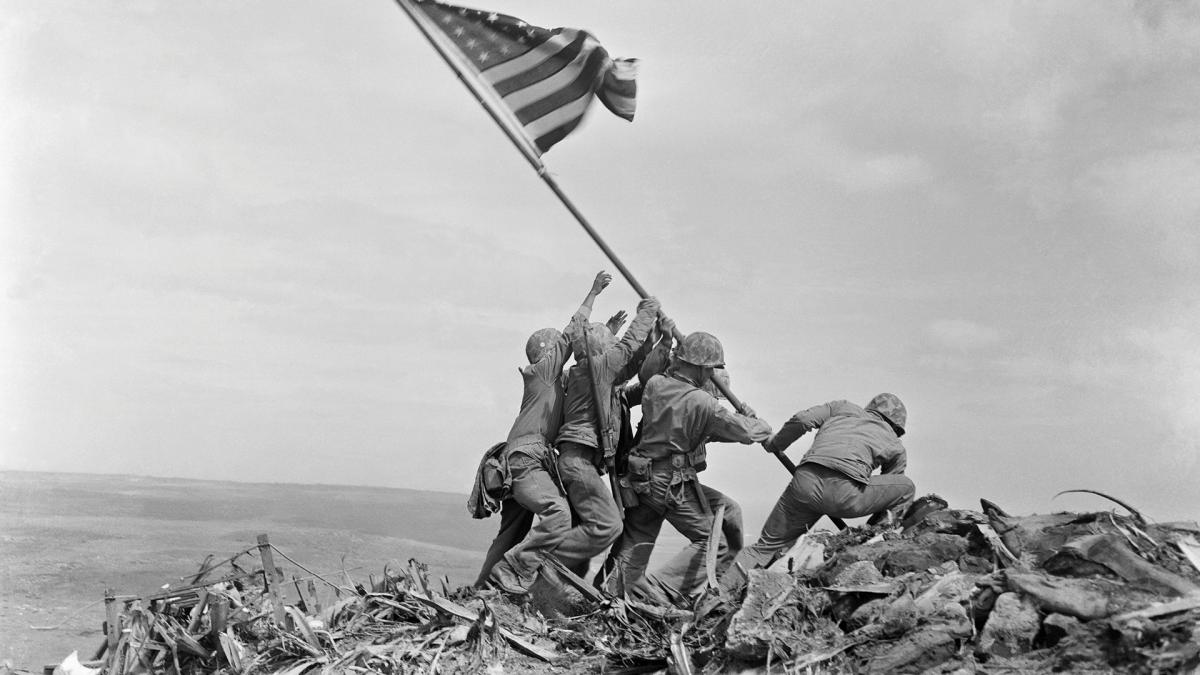 Six soldiers raise the American flag atop a rocky hill during the Battle of Iwo Jima in World War II.