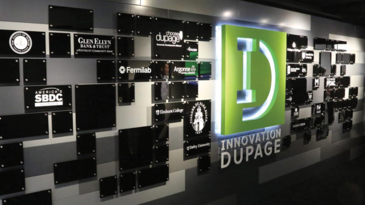 Illuminated Innovation DuPage logo on wall with various partner logos on black plaques.