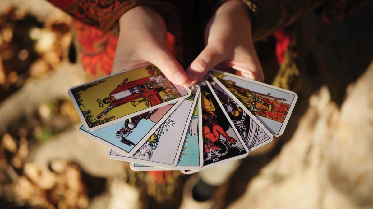 Person holding a fan of colorful tarot cards outdoors in bright sunlight.