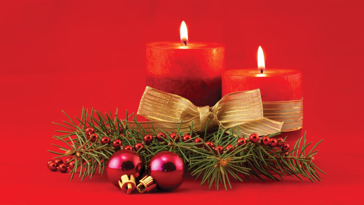 Two red candles with gold ribbon, pine branches, and red ornaments on a red background.